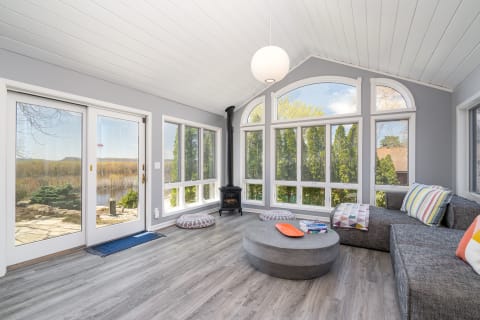 A bright sunroom featuring large windows, gray sectional sofa, and a scenic outdoor view.