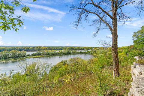 A scenic landscape of a river bends through green and autumn-colored trees under a clear blue sky.