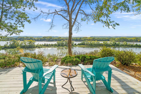 Two turquoise Adirondack chairs on a deck overlooking a peaceful river and lush greenery.