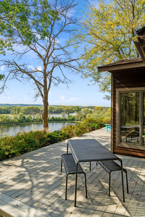 Outdoor deck with a black table and chairs overlooking a river and trees.