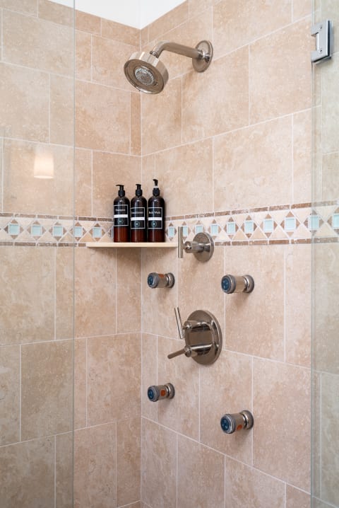 Modern shower featuring beige tiled walls, a rain showerhead, and dark amber shampoo bottles.