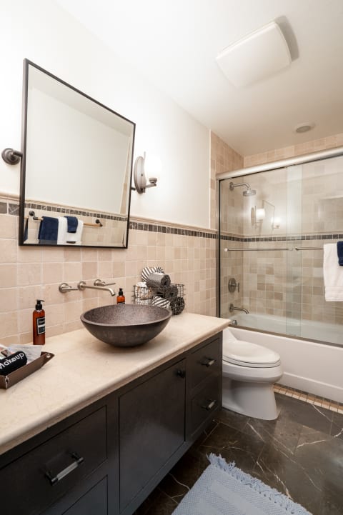 Modern bathroom with a dark vanity, round stone sink, and glass shower.