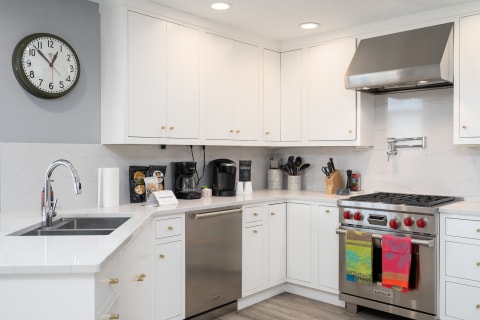Modern kitchen with U-shaped white quartz countertops, stainless steel appliances, and organized items.
