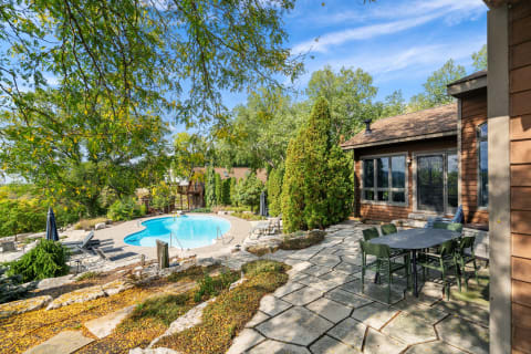 A serene backyard with a swimming pool and dining area surrounded by trees and autumn leaves.