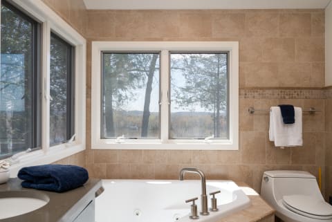 Modern bathroom with windows offering a view, featuring a bathtub and towels.
