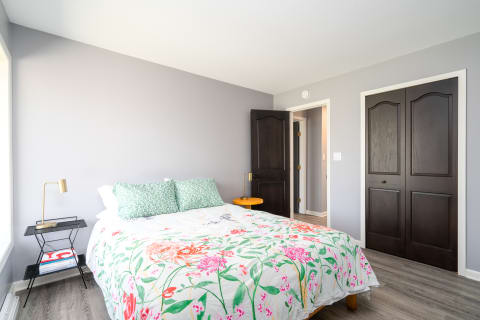 A cozy bedroom with a floral bedspread, colorful pillows, and modern furniture.
