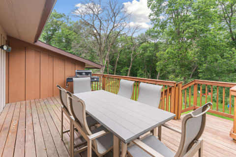 Outdoor deck featuring a dining table and chairs, with a grill and surrounding trees.