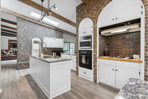 Modern kitchen with granite island, white cabinetry, and exposed brick wall.