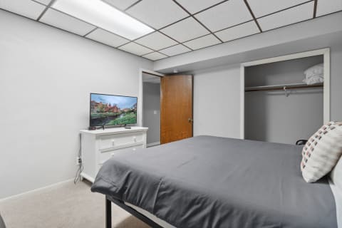 A simple bedroom with gray bedding, a TV on a white dresser, and a wooden closet door.