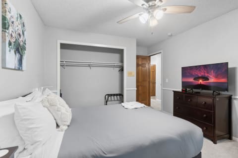 A modern bedroom with a bed, dresser with a TV, and closet space.