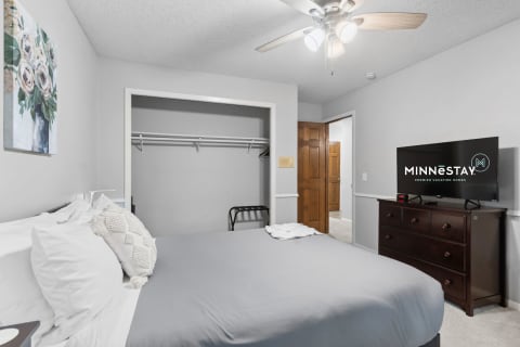 A cozy bedroom with a bed, dresser, television, and closet.