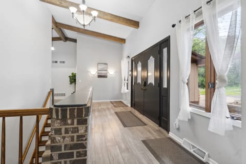 A spacious entryway with wooden beams, black front doors, and large windows draped with sheer curtains.