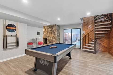 A stylish game room with a billiard table, stone fireplace, and Pac-Man sign.