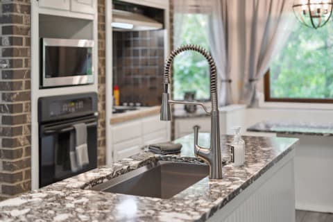 A modern kitchen featuring a stainless steel faucet, granite countertop, and white cabinetry.