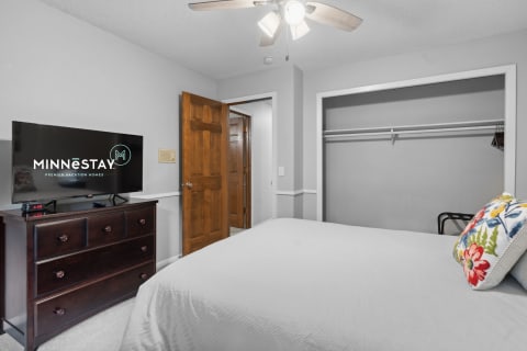 A cozy bedroom featuring a bed, a wooden dresser, and a TV with the MINNESTAY logo.