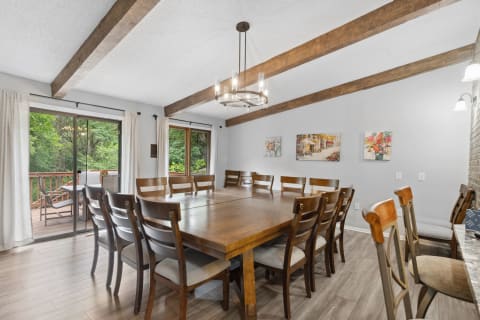 A spacious dining area featuring a large wooden table, surrounded by chairs, with access to an outdoor deck through sliding glass doors.