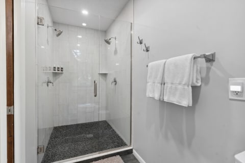 Modern bathroom with glass shower, pebble floor, and white towels.