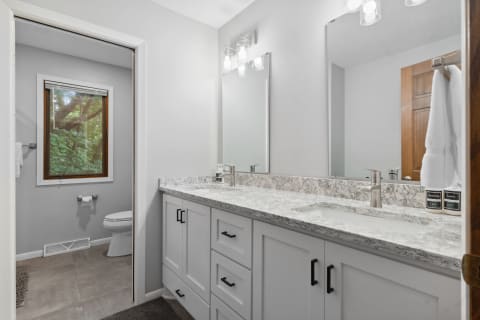 Modern bathroom featuring a double sink vanity, large mirrors, and a window with greenery view.
