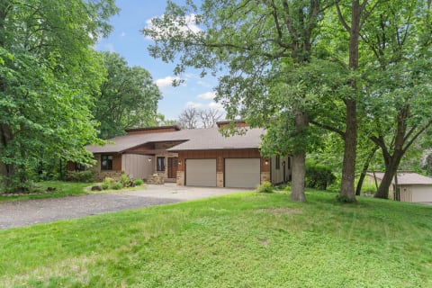 A contemporary single-story house with stone and wood siding, surrounded by trees and grass.