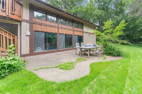 Outdoor patio of a house with a table and chairs by a green lawn.