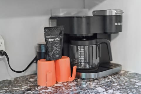 A coffee maker and orange mugs on a granite countertop.