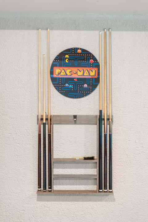 Wall-mounted display of pool cues with a colorful Pac-Man sign.