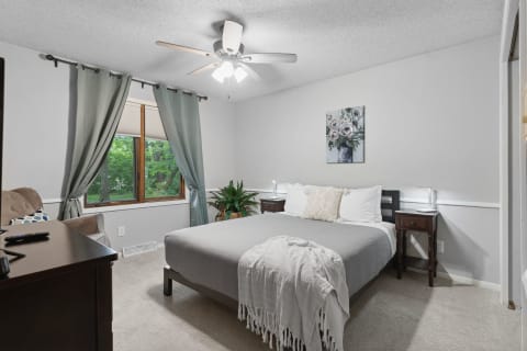 Cozy bedroom with a bed, floral wall art, and green curtains overlooking greenery outside.