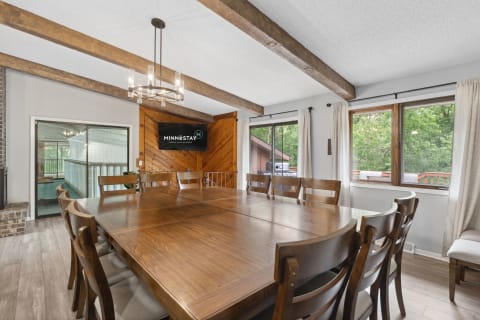 A modern dining room with a large wooden table, chairs, and a television mounted on the wall.