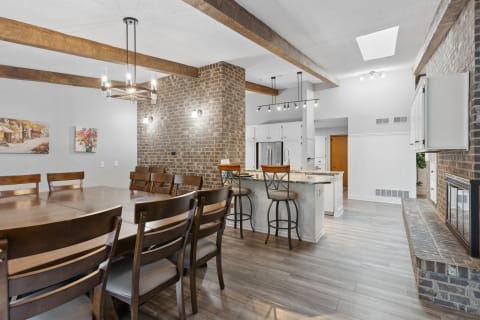 A modern kitchen and dining space with wooden beams, dining table, and brick walls.