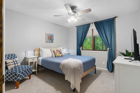 Cozy bedroom with blue accents, floral decor, and a view of greenery through a window.