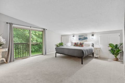 Modern bedroom featuring a gray bed, colorful pillows, and a view of greenery through glass doors.