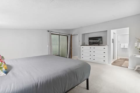 Modern bedroom with gray duvet, white dresser, and large glass doors.