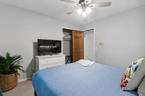 Cozy bedroom with blue bedspread and a flat-screen TV on a white dresser.