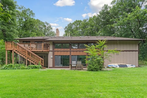 Two-story wooden home with a deck and spacious lawn under a blue sky.