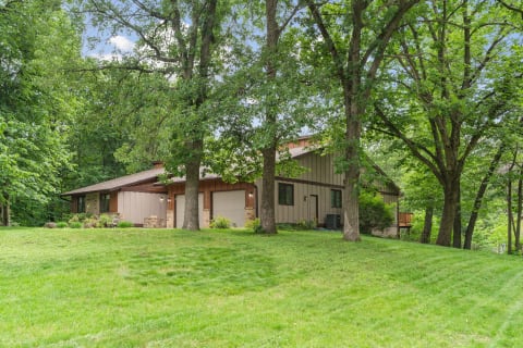 A brown and beige modern house surrounded by trees and a green lawn.