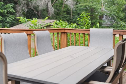 A wooden deck with a gray table and chairs set in a lush green garden.