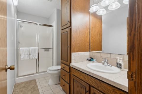 A well-organized bathroom with a shower, wooden cabinets, and a white sink.