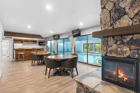 Interior space with a fireplace, dining area, and view of a pool through large glass windows.