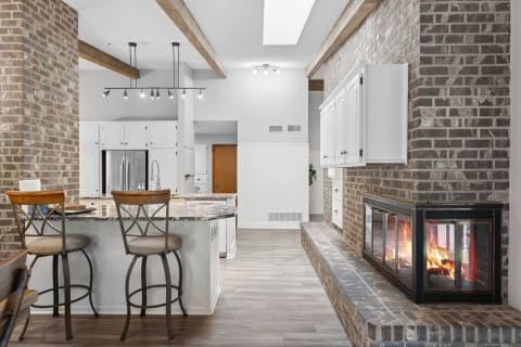 An inviting modern kitchen featuring a central island, bar stools, and a brick wall fireplace.