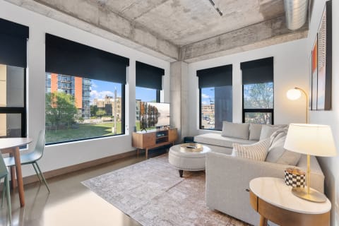 A stylish living room with a gray sofa, TV, and large windows overlooking a cityscape.