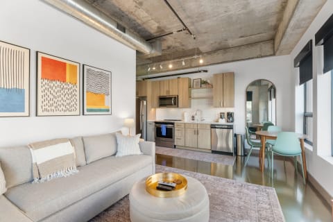 Modern apartment interior with a gray sofa, abstract art, and a sleek kitchen.