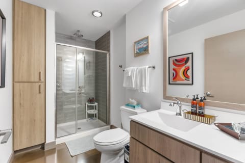 A contemporary bathroom featuring a glass shower, wooden cabinet, and stylish vanity with toiletries.