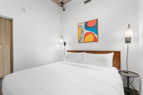 Modern bedroom with white bed linens, wooden headboard, and colorful abstract artwork.