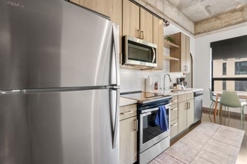 Modern kitchen with stainless steel fridge, black oven, and wooden cabinets.