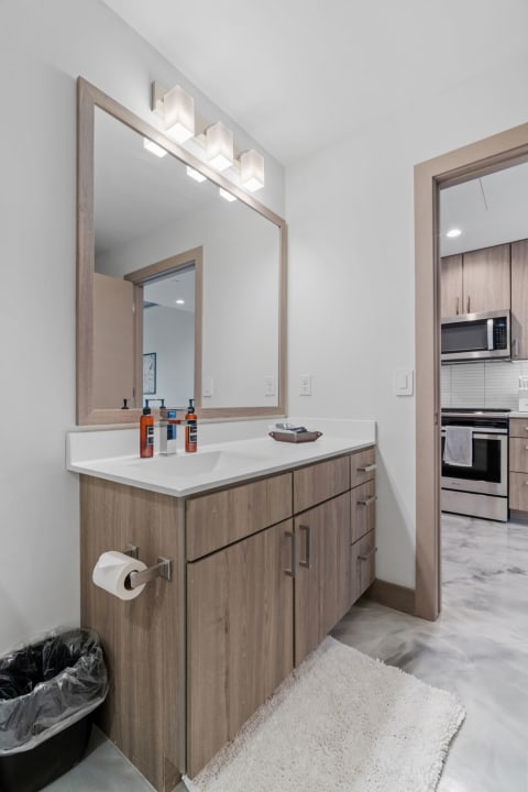 A contemporary bathroom featuring a wooden vanity, large mirror, and modern lighting fixtures.
