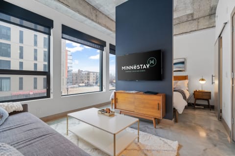 Contemporary living room featuring a gray sofa, coffee table, and urban views from large windows.