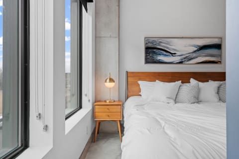 A well-designed modern bedroom featuring a bed, nightstand, and large windows with abstract art.
