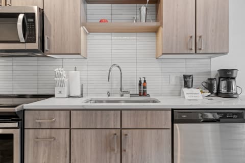 Modern kitchen with wood cabinetry, stainless steel appliances, and a white countertop.