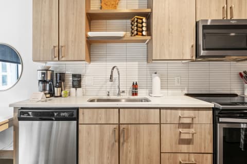 A stylish kitchen featuring light wood cabinetry, a stainless steel sink, and various countertop appliances.