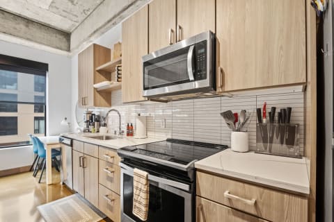 A modern kitchen featuring light wood cabinets, black appliances, and a window view.